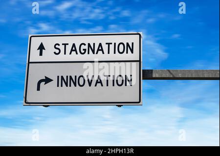 Road sign with words stagnation and innovation. White two street signs with arrow on metal pole on blue sky background. Stock Photo