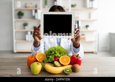Black nutritionist holding digital tablet with blank screen, demonstrating mockup for website or app design Stock Photo