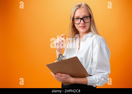 Teen school girl taking notes on clipboard against orange background Stock Photo