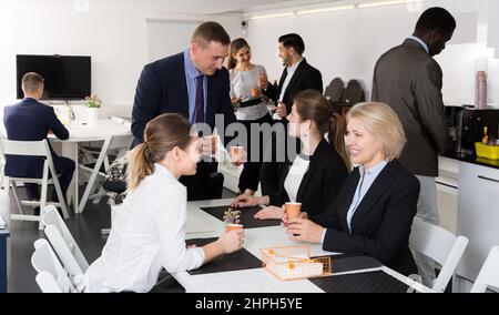 Cheerful multinational work team having break at office, drinking coffee and talking Stock Photo