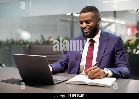 Happy black businessman using laptop and taking notes Stock Photo