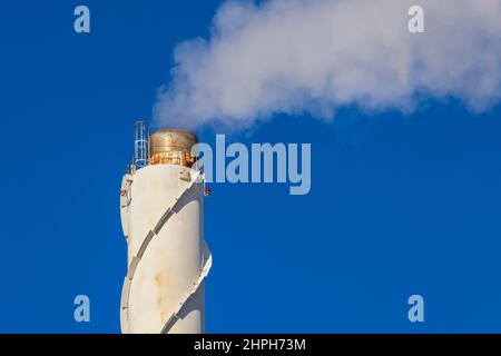 Close up view of smoke coming out of chimney against blue sky. Ecology and greenhouse effect concept. Sweden. Stock Photo