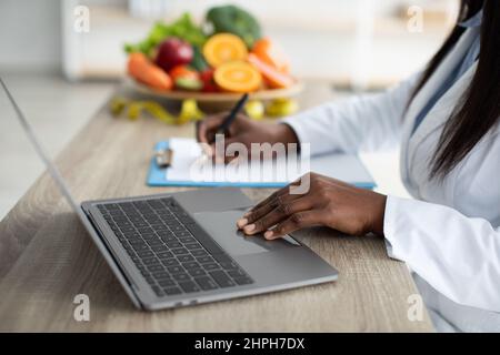 Working process. African american dietitian creating diet plan for patient or counting calories, working on laptop Stock Photo