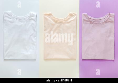 Multicolored t shirts pastel colors Pink White Purple Mockup for design on color background. Stacked Basic t shirts clothes trendy Minimalistic Stock Photo