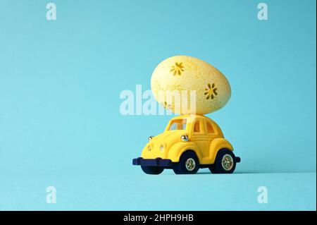 One Easter egg on a small car on a blue background. Copy space. Easter card. Stock Photo