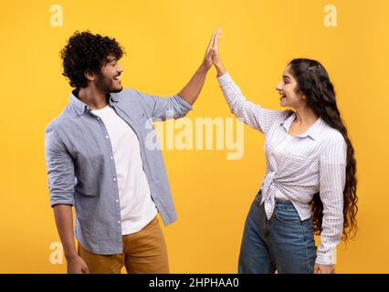 Common success. Young excited indian couple giving high-five, clapping hands, greeting each other over yellow background Stock Photo