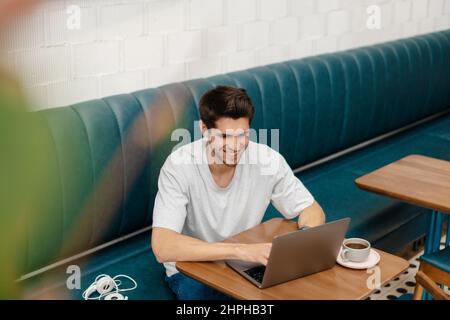 Smiling young man student sitting in cafe indoors with laptop computer Stock Photo