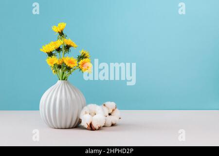 Yellow dandelions in vase on cyan background, close up, copy space. Bouquet sunny wildflowers dandelions in ceramic vase in bright background. Stock Photo