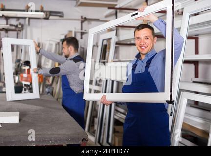 Production workers in coverall with different finished PVC profiles and windows at factory Stock Photo