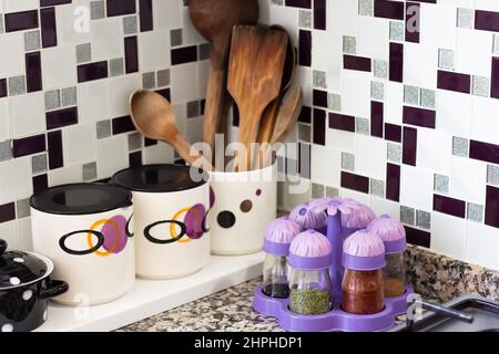 Kitchen utensils, wooden spoons, spice jars, organization and storage containers on kitchen countertops with granite surface and ceramic background Stock Photo