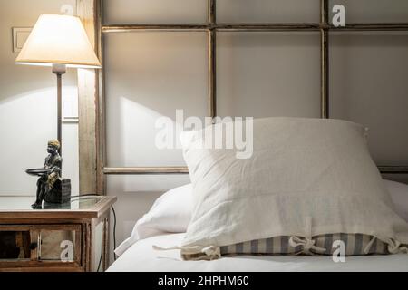 Wooden headboard of designer bed with cushions and lamp with a figure as a staff on the bedside table Stock Photo