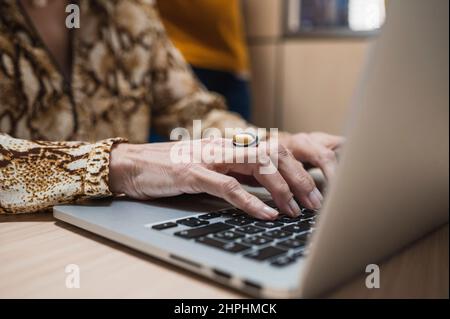 Close up of senior woman hands typing on laptop in an office. Stock Photo