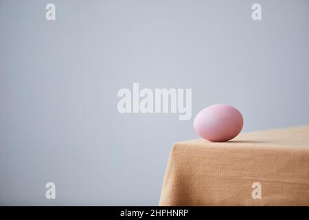 Minimal shot of single Easter egg placed on cozy dinner table, graphic Spring background, copy space Stock Photo