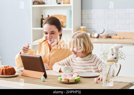 Portrait of happy mother enjoying breakfast with cute son and using tablet in kitchen, copy space Stock Photo