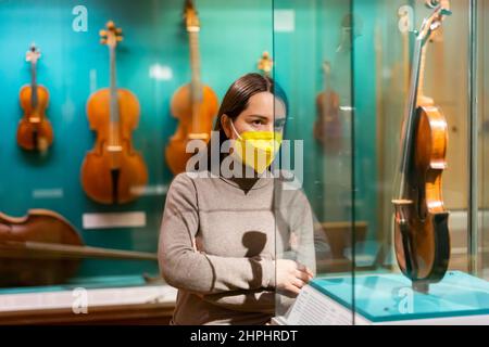Female museum visitor in mask examining ancient musical instruments Stock Photo
