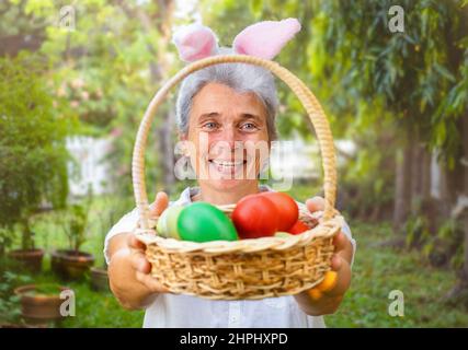 Senior woman holding out Easter basket with eggs in the backyard Stock Photo