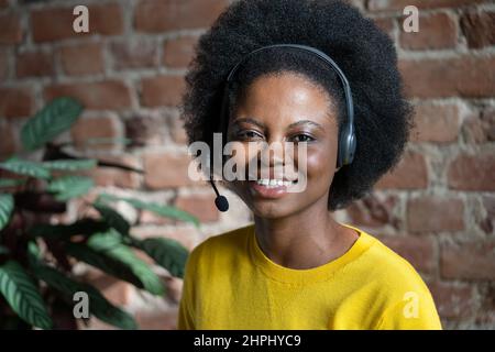 Happy Black woman with headset posing over brick wall, look at camera. Call centre operator. Stock Photo