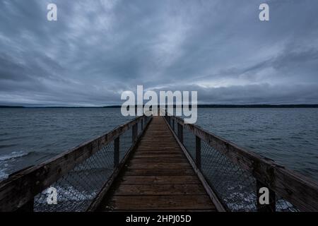 Long boardwalk pier into horizon over ocean under dramatic overcast sky