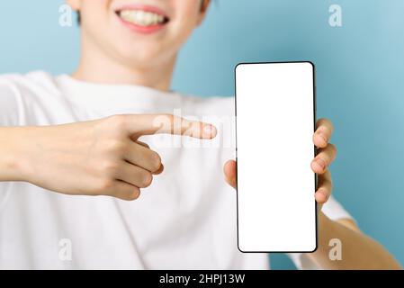 Happy smiling boy showing smartphone mockup in a blue backdrop. blank cellphone screen Stock Photo