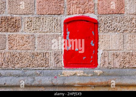 A small metal box painted red embedded in a brick wall Stock Photo