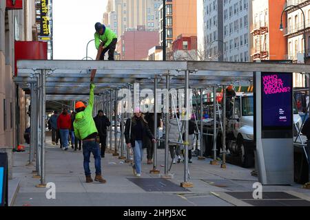 Workers lift heavy iron support beams onto sidewalk scaffolding under construction on a New York City street with people walking underneath Stock Photo