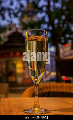 A flute of sparkling cava wine at an al fresco bar in the center of Madrid, Spain with ornate old buildings and trees in the background at sunset Stock Photo
