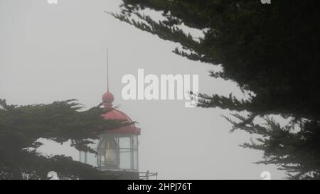 Point Pinos old historic lighthouse fresnel lens glowing, foggy rainy bad weather. Illuminated retro vintage light house or beacon tower, misty cypress pine tree forest. Monterey, California coast USA Stock Photo