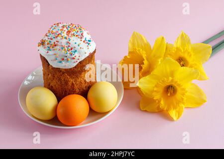 Easter cake, eggs and daffodil flowers on pink background. Stock Photo