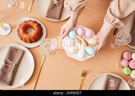 Top view close up of young woman putting cute Easter eggs platter on dinner table decorated for Spring, copy space Stock Photo