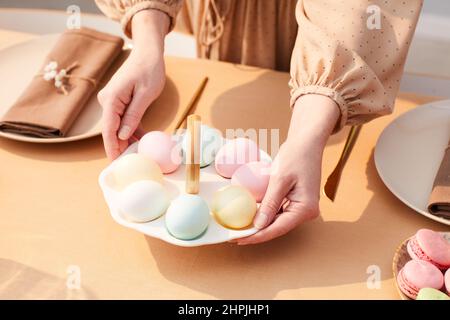 Close up of young woman putting cute Easter eggs plate on dinner table decorated for Spring, copy space