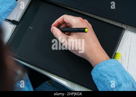 designer working on a professional tablet with a pen, Close-up of a man's hand holding a graphic pen for drawing Stock Photo