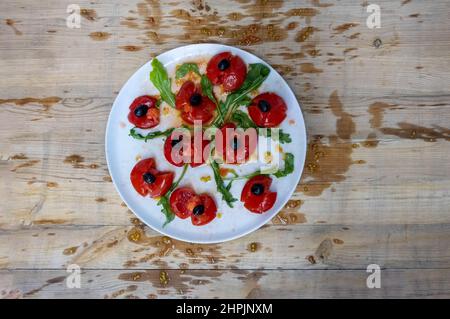 Tomatoes smashed with a fist, decorated with black olives and arugula arranged on a wooden table, the pulp splattered wildly, are supposed to represen Stock Photo