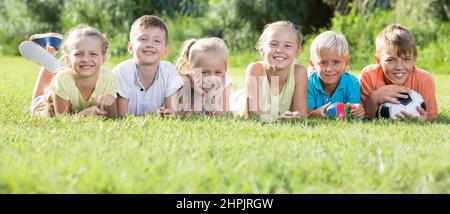 Group of friendly kids lying on green grass in park Stock Photo