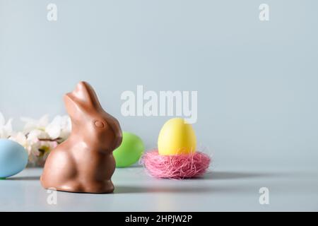 Easter pink egg in nest and chocolate bunny in spring composition on blue background. Happy Easter greeting card. Stock Photo