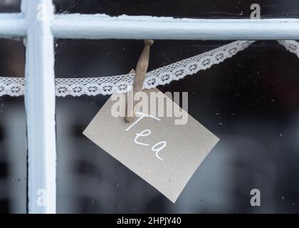 Tea sign pegged to lace in shop window advertising hot drinks to customers of takeaway cafe Stock Photo