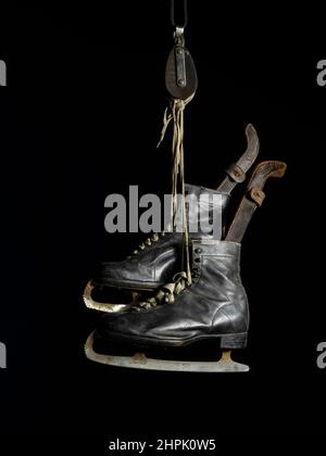 Pair of vintage Ice Skates with leather boots and blade guards suspended from a pulley wheel Stock Photo
