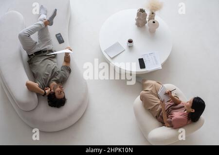 Overview of two young specialists in casualwear discussing financial data while woman making notes and man analyzing information Stock Photo