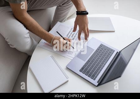Hands of young economist or analyst with pen pointing at financial document while analyzing data in front of laptop by table Stock Photo