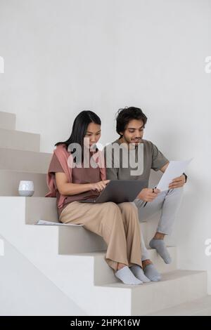 Happy young businessman with financial document sitting by female colleague with laptop making presentation of online data Stock Photo