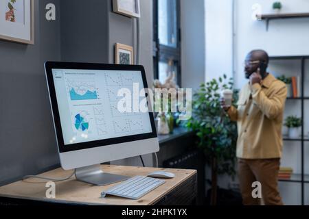 Computer monitor on desk with digital financial diagram and graphs on screen on background of young businessman calling Stock Photo