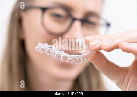 smiling woman using clear plastic removable braces aligner or whitening tray. dental orthodontic care Stock Photo