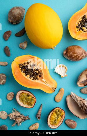 Ripe cut papaya, melon, passion fruit, seashells, pebbles on blue pastel background. Top view, flat lay, close up. Tropical, healthy food, vacation, h Stock Photo