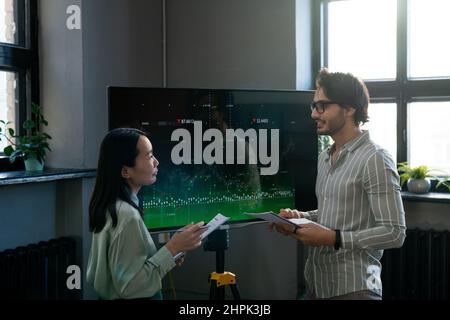 Two young confident analysts with documents discussing interactive financial data while businessman explaining something to female colleague Stock Photo