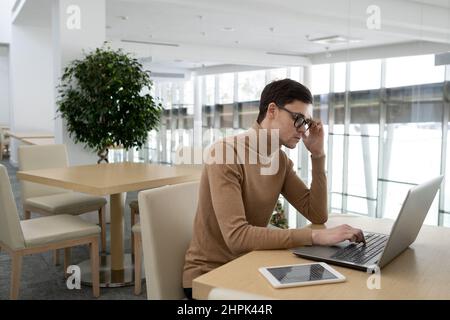Young businessman concentrating on work over new project while sitting in front of laptop by desk in office of modern technology company Stock Photo