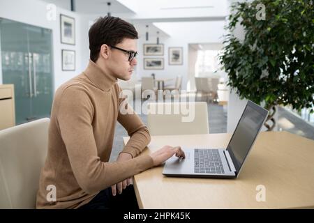 Young serious entrepreneur in casual clothes sitting in front of laptop while working over development of new programming Stock Photo
