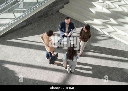 Group of contemporary delegates in formalwear having discussion of new strategies and plans while standing in lounge of business center Stock Photo