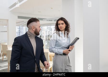 Young serious businesswoman with documents listening to ceo during discussion of working questions while moving along office Stock Photo