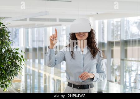 Happy young contemporary gaming developer in vr headset pointing at virtual screen while making presentation of new high tech space Stock Photo