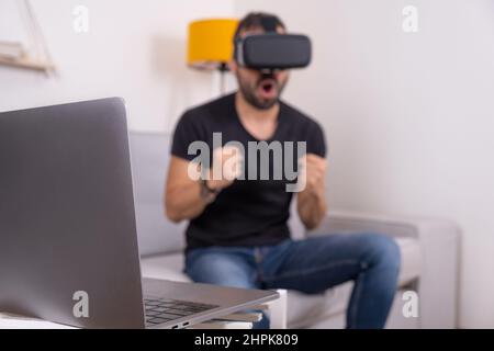 Young man in VR glasses headset at home with laptop , future technology, education video gaming Stock Photo