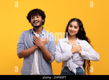 Thankful indian couple keeping both palms on chest, smiling at camera, expressing appreciation and kindness Stock Photo